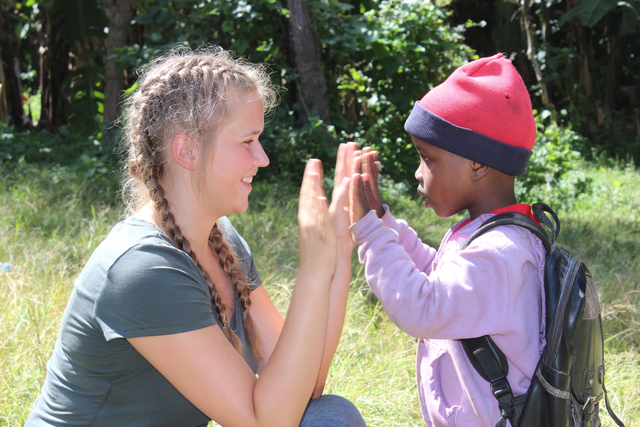 Projects Abroad volunter high fives child outside a Childcare placement in Tanzania. Female volunteer working with children in Tanzania high fives a young boy outside a care centre.